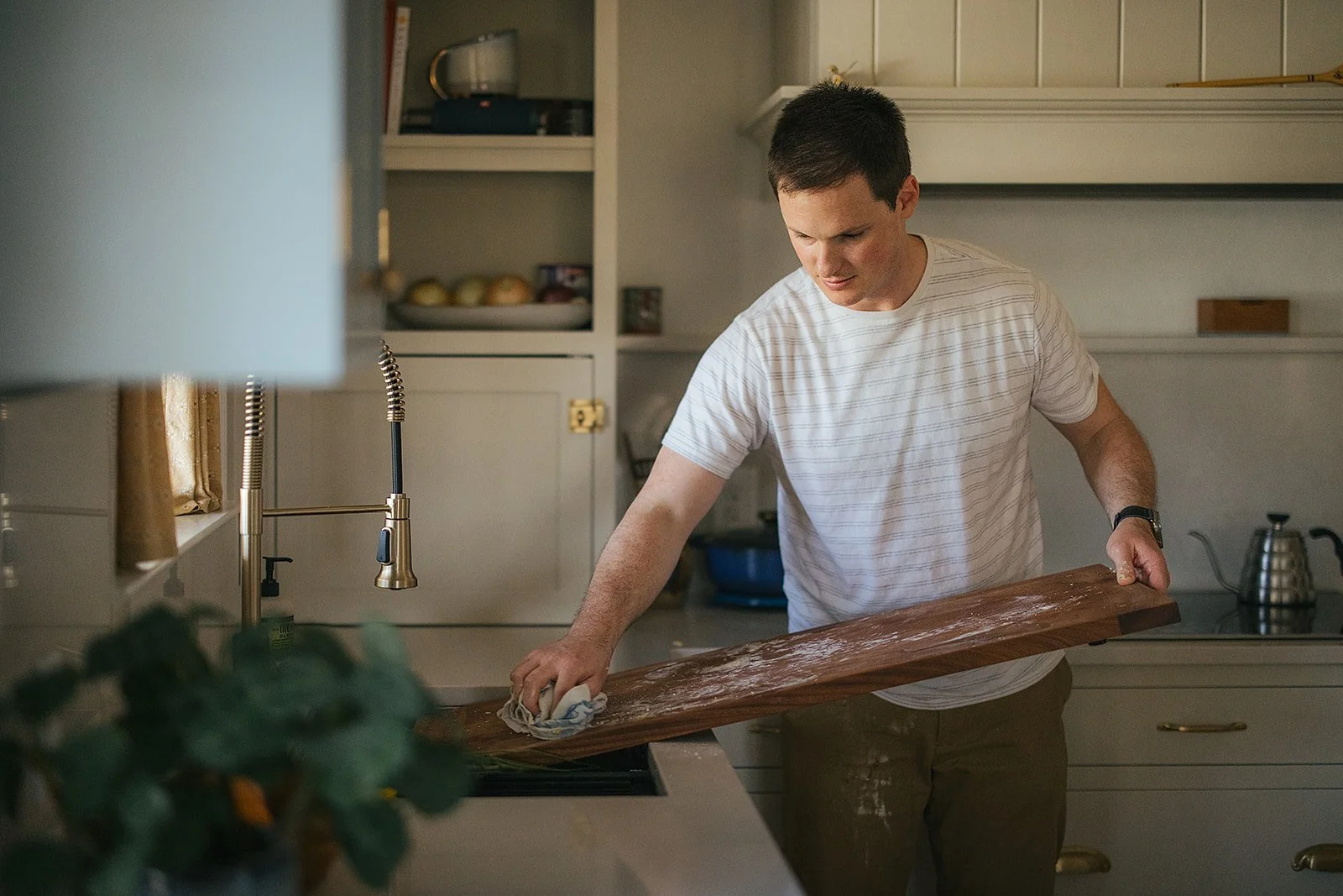 Dad cleans wooden cutting board at kitchen sink — an everyday moment captured during Durham in-home family photography session