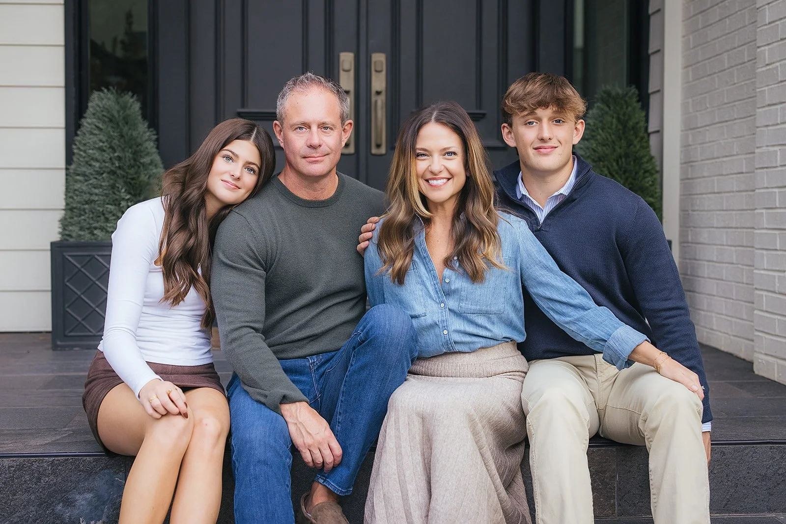 A family of four sits together on the front steps of their downtown Raleigh, NC home, smiling warmly at the camera in a classic front-door portrait.