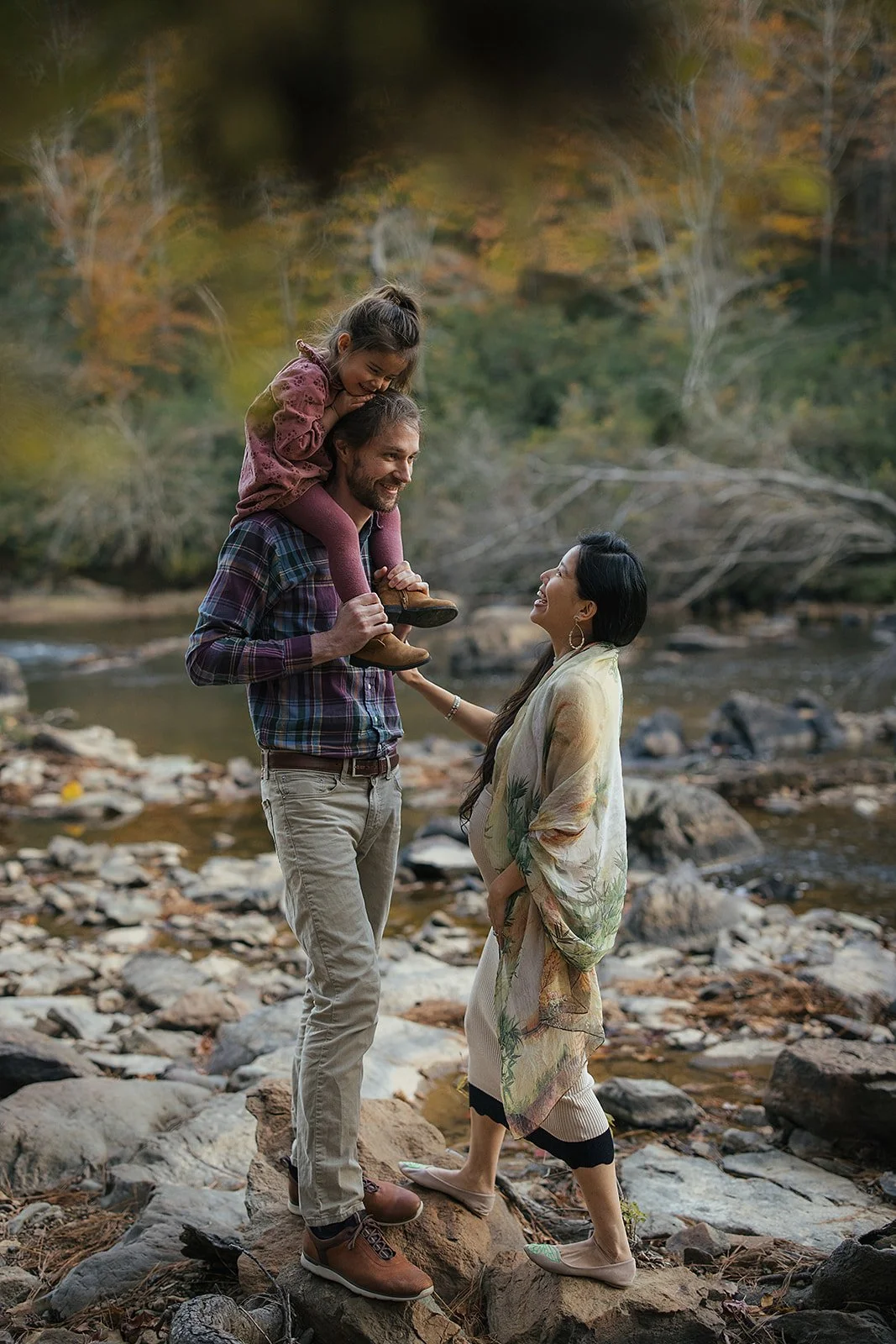 a pregnant mother with her child and husband play on the Eno River during a maternity photoshoot