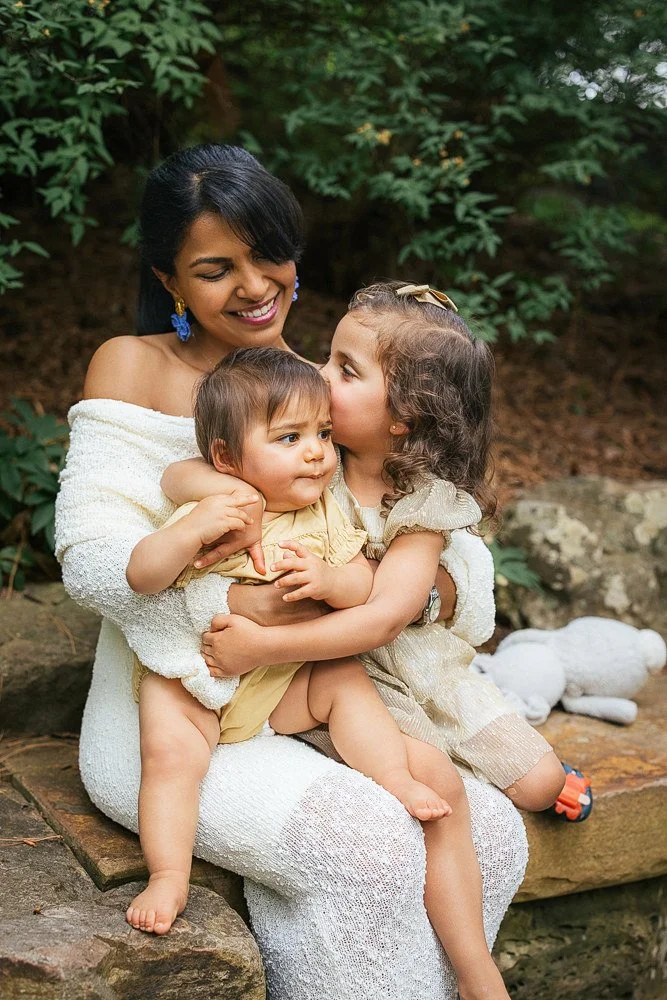 Mother holds two children on a stone wall for a family photo session at Duke Gardens in Durham, NC