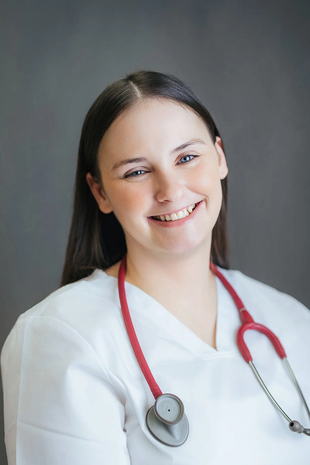 Durham Tech nursing student with long dark brown hair, warm smile in white scrubs and red stethoscope, professional nursing headshot Durham NC