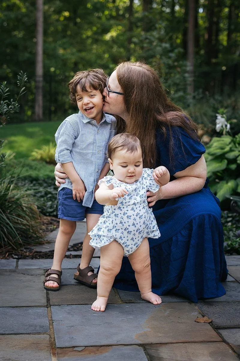 Mom kissing toddler's cheek while holding baby outside