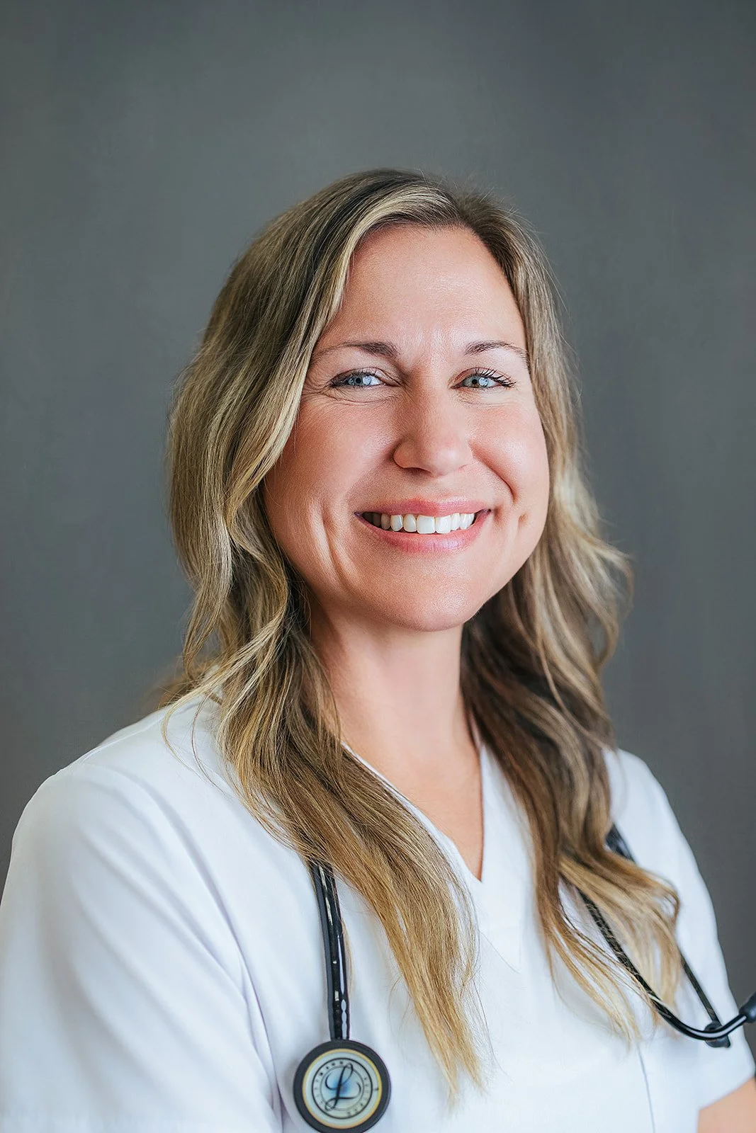 Durham Tech nursing student with long wavy blonde hair, warm smile in white scrubs and black stethoscope, professional headshot by Fifty Two Hundred Photography