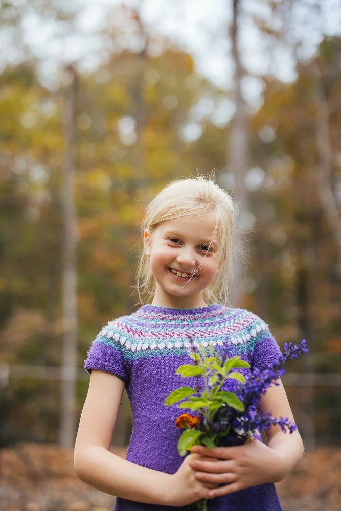 Young girl smiling in purple dress with flowers she picked