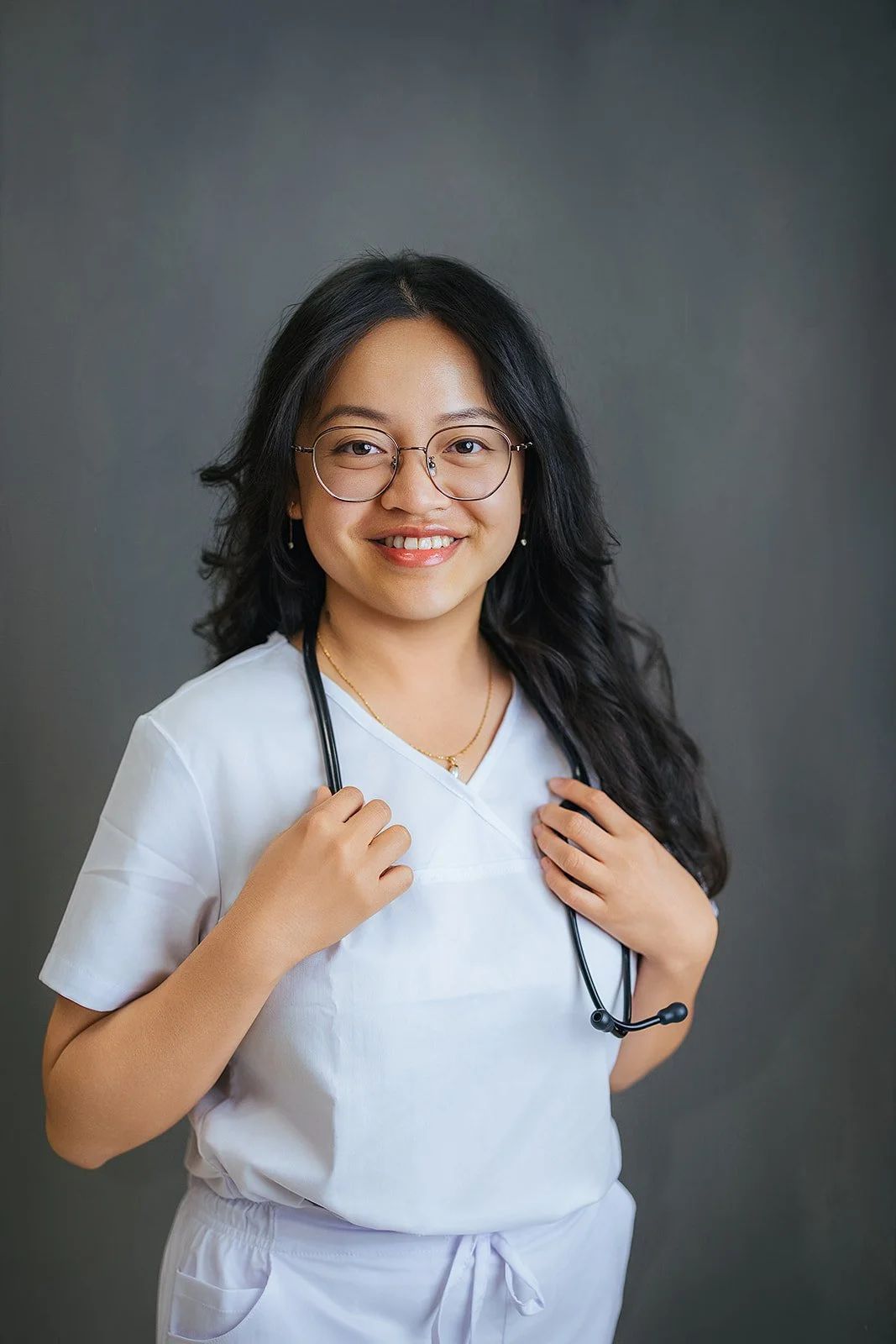 Durham Tech nursing student with glasses holding her stethoscope and smiling, white scrubs, professional headshot by Fifty Two Hundred Photography Durham NC