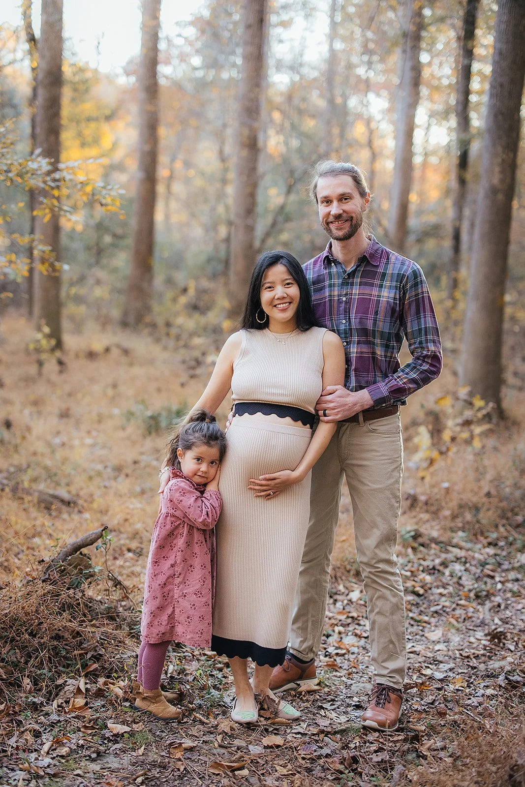 A pregnant woman poses with her family on the Eno River for a maternity photoshoot