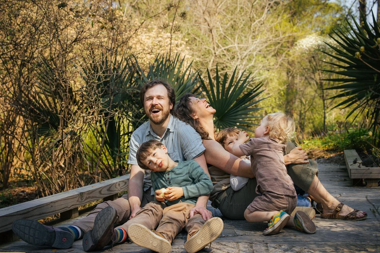 Three boys tumbling and piling over their parents on the wooden boardwalk at Duke Gardens while dad laughs — Durham NC family photographer