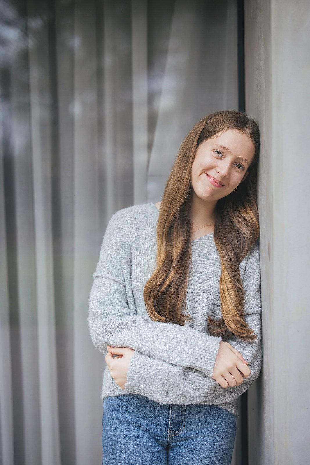 Young Girl in Grey Sweater Smiling Leaning Against Wall