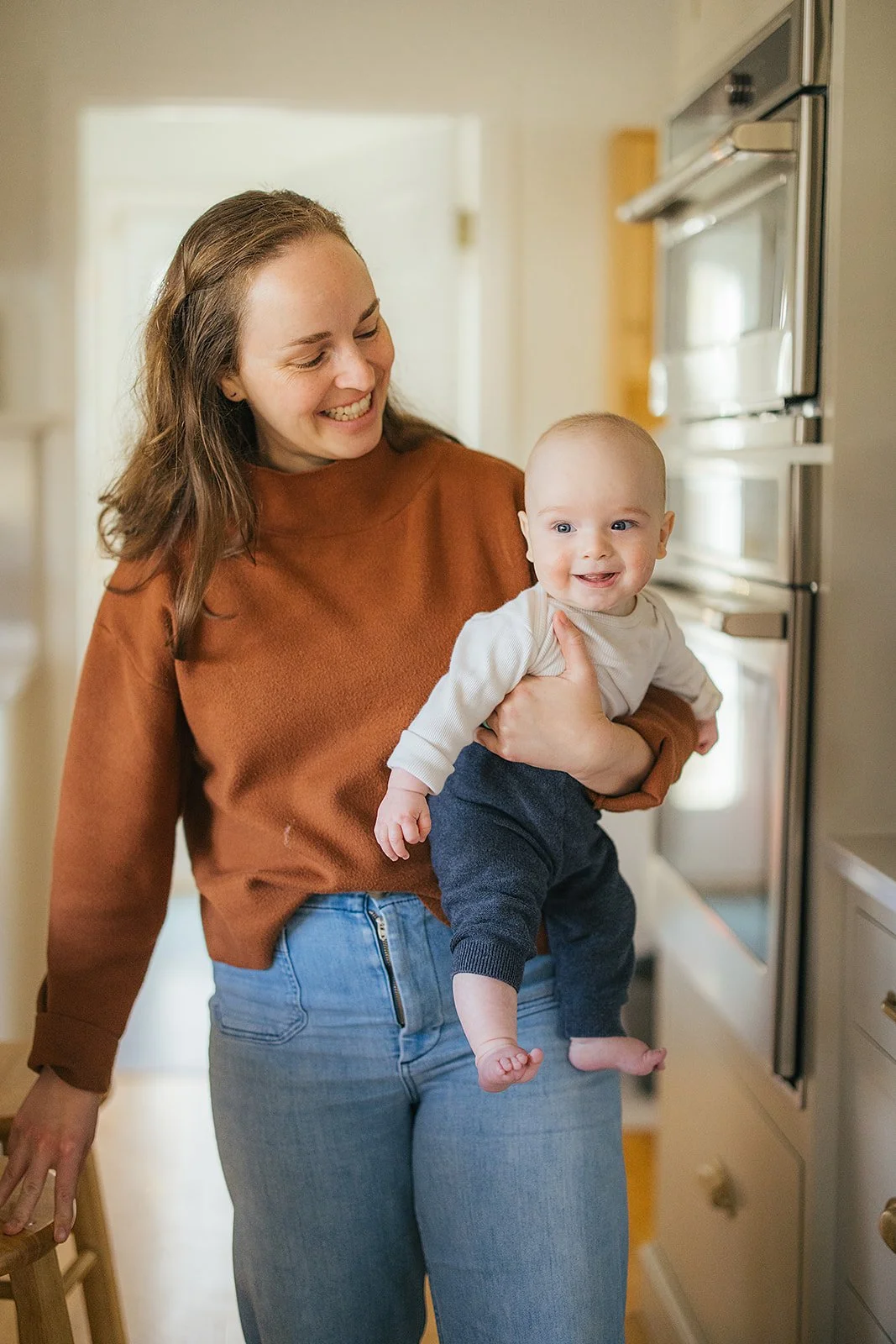 Mom holds her smiling baby in the kitchen during Durham lifestyle family photography session