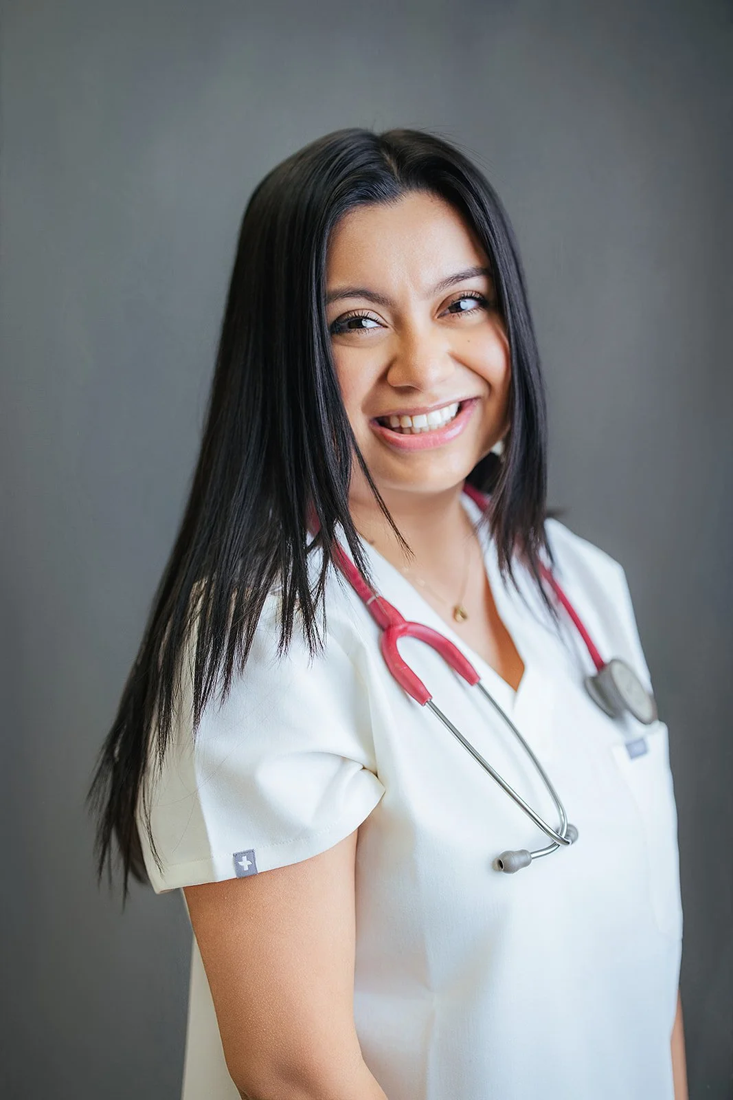 Durham Tech nursing student with long straight dark hair, bright joyful expression in white scrubs and red stethoscope, professional headshot Durham NC