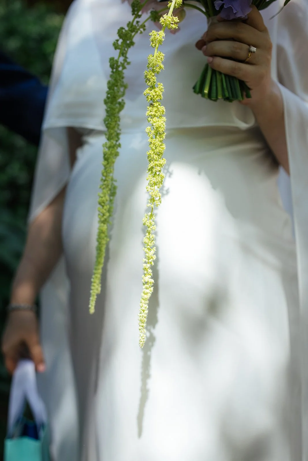 Close-up detail of trailing green amaranthus draping from a bridal bouquet held against a white wedding dress, Durham NC wedding