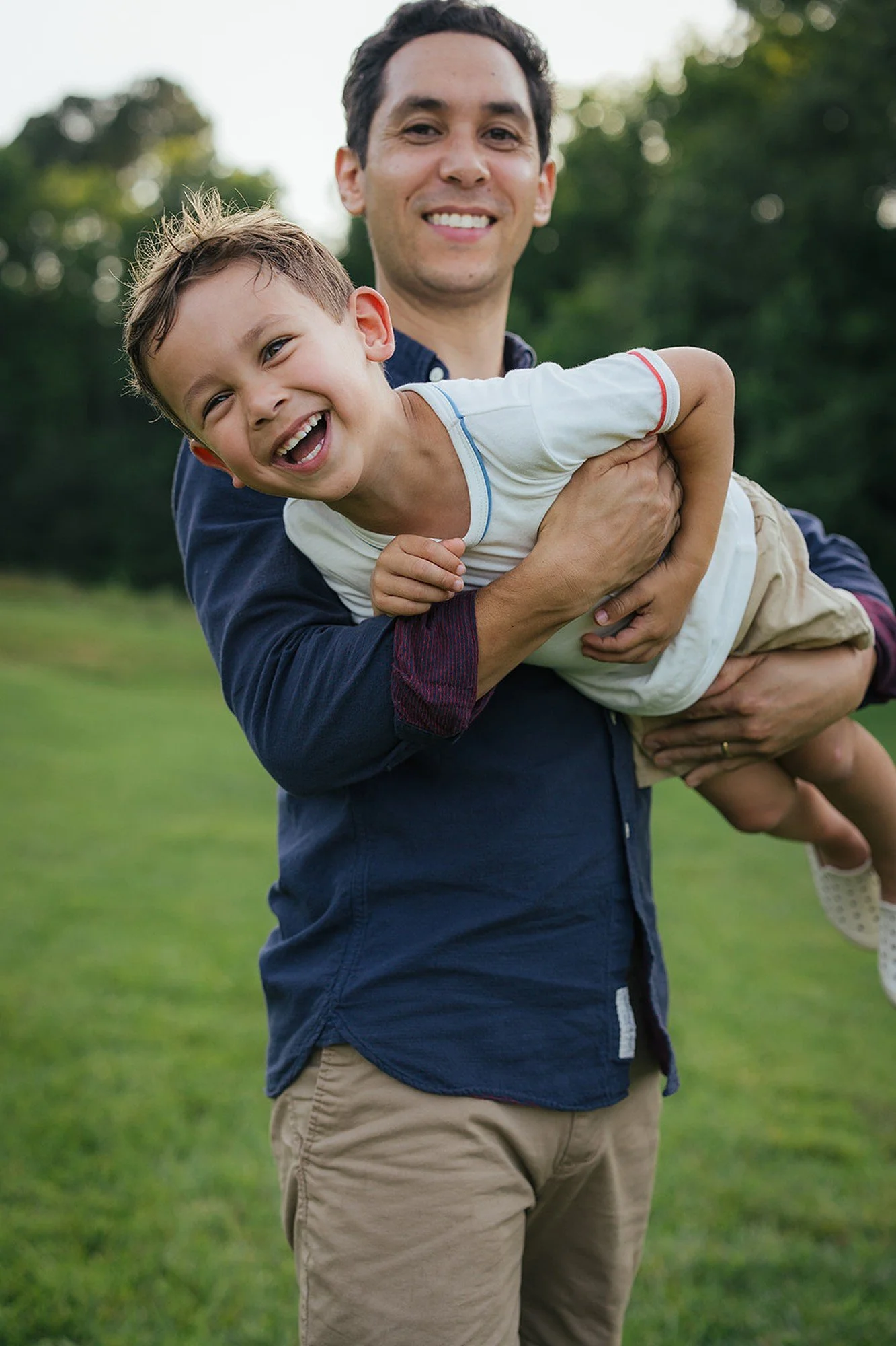 Father and son smile for a family photo session in Durham NC with a green background