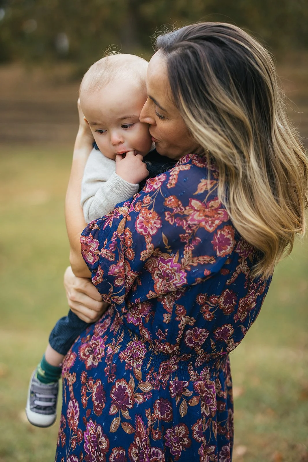 Mom kisses her baby boy's head in a tender side profile portrait during Durham NC motherhood photography session at Duke Park