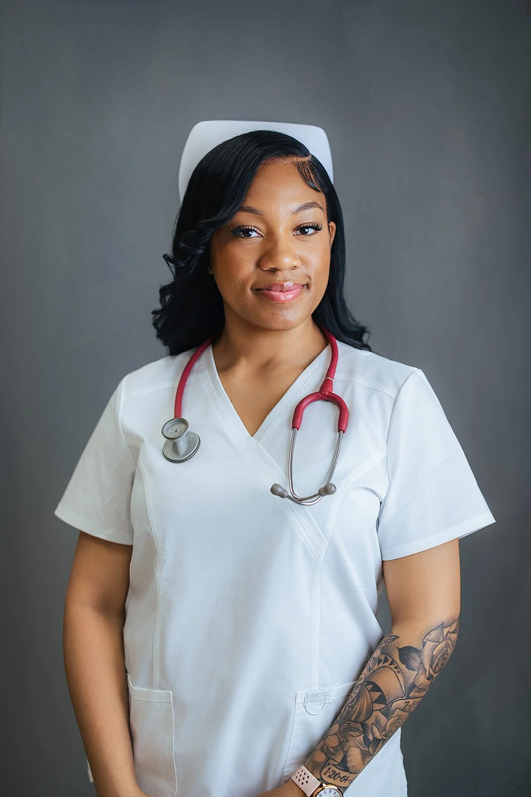 Durham Tech nursing student with floral arm tattoo, wearing white scrubs and red stethoscope, soft confident smile in professional headshot