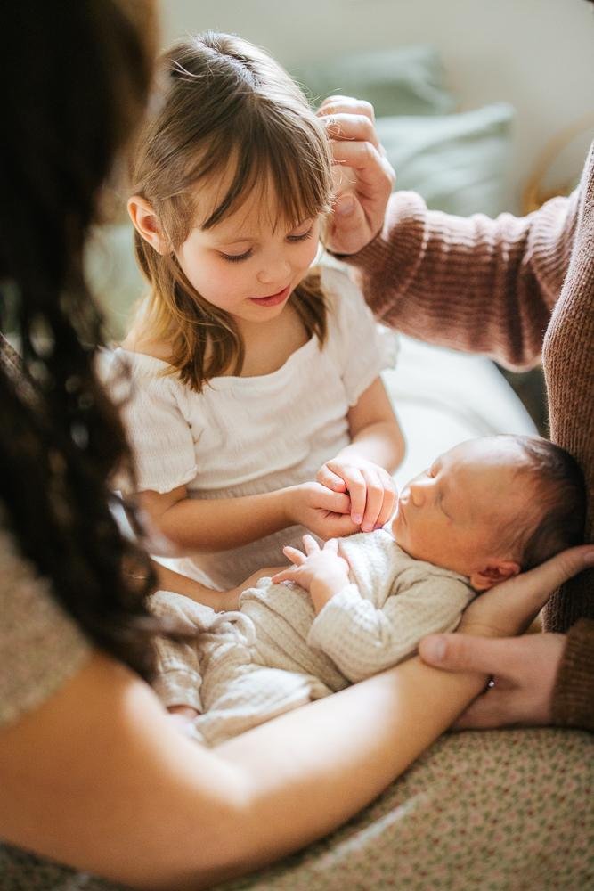 Toddler big sister gently touching the hand of her newborn baby brother during an in-home lifestyle session in Durham NC