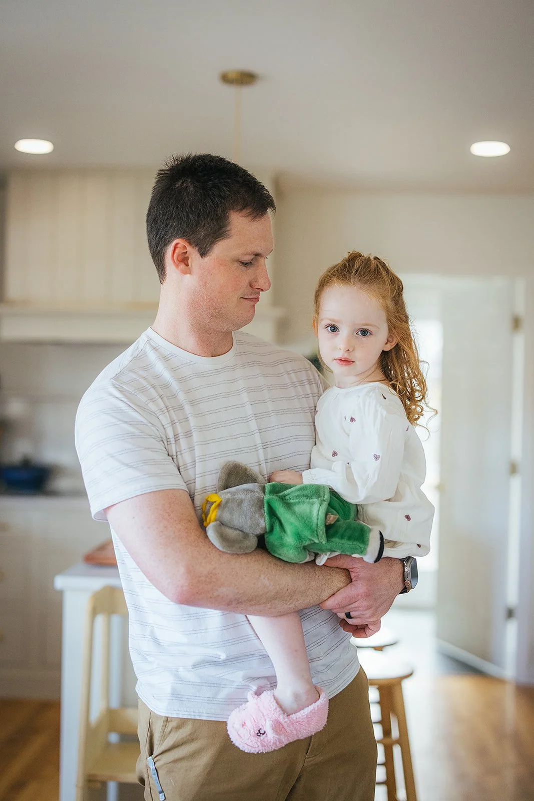 Dad holds toddler daughter in arms in kitchen during Durham in-home family photography session