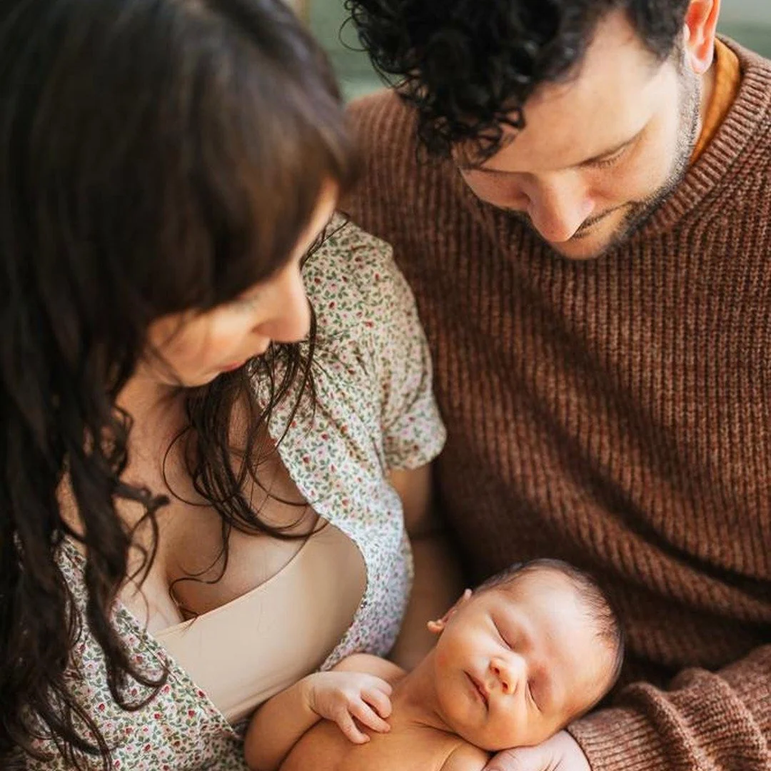 Mother and father look down on their sleeping newborn during an in home photoshoot in Durham, NC