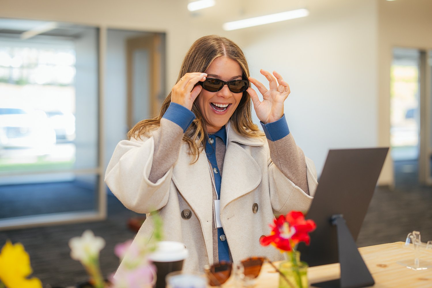 Woman in white coat laughing while trying on sunglasses at a branded activity table at a corporate event at Longfellow Triangle LIFE in Raleigh NC