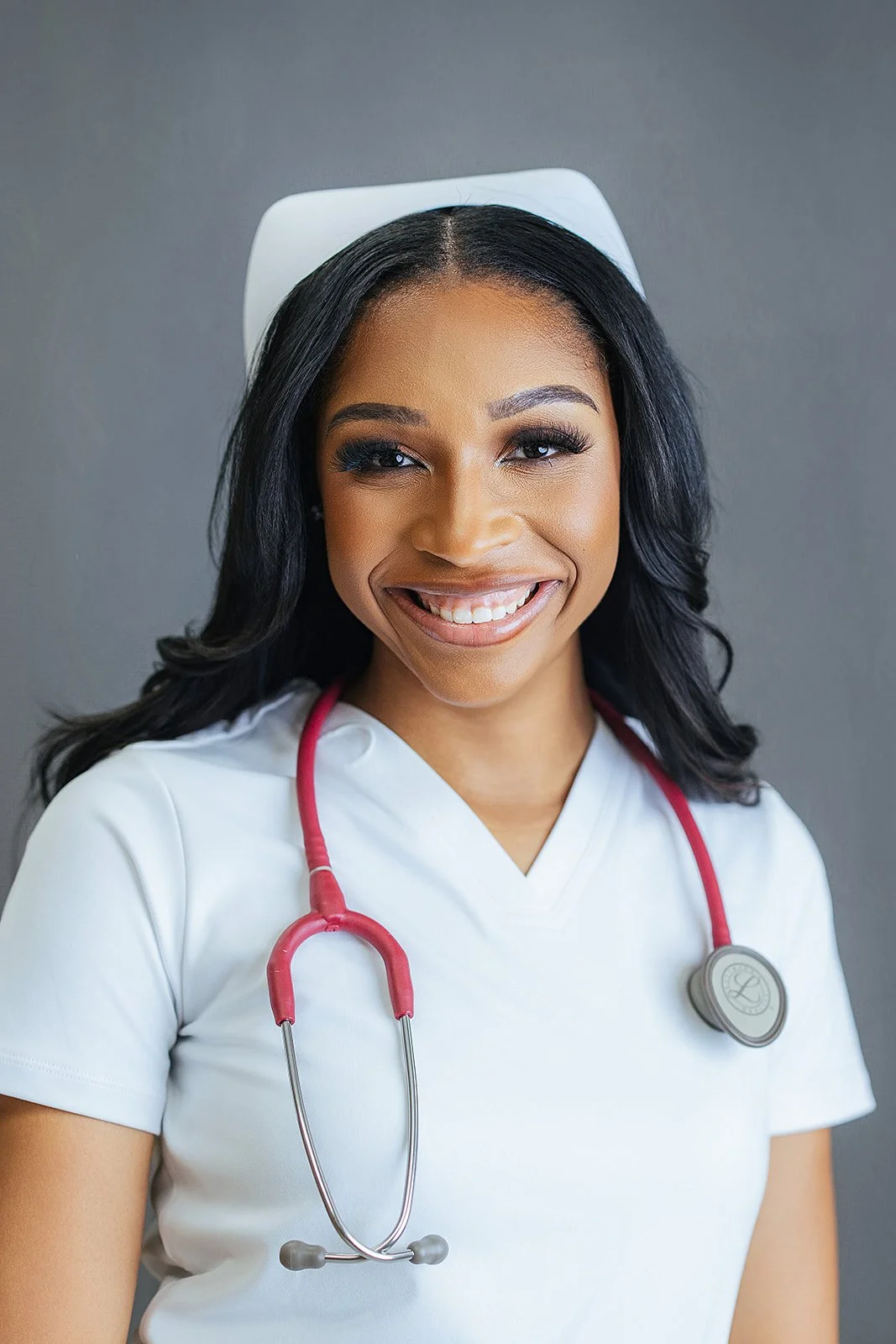 Durham Tech nursing student in white nurse cap and white scrubs with red stethoscope, bright joyful smile, professional headshot in Durham NC