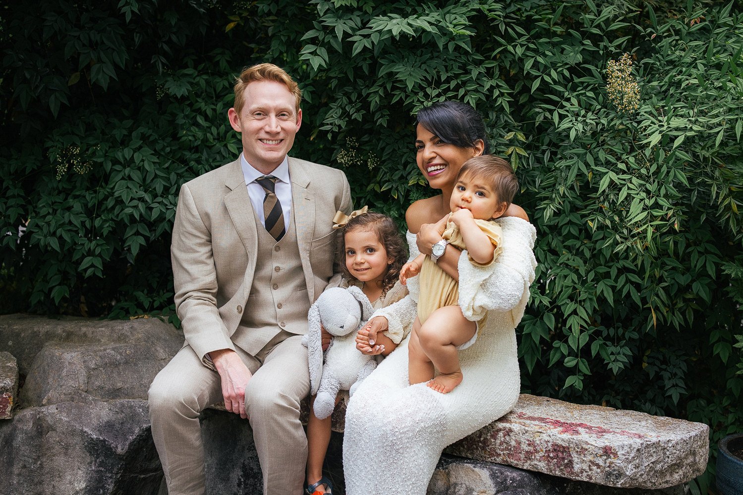 Family of four snuggles on a stone wall during a family photoshoot at Duke Gardens in Durham NC