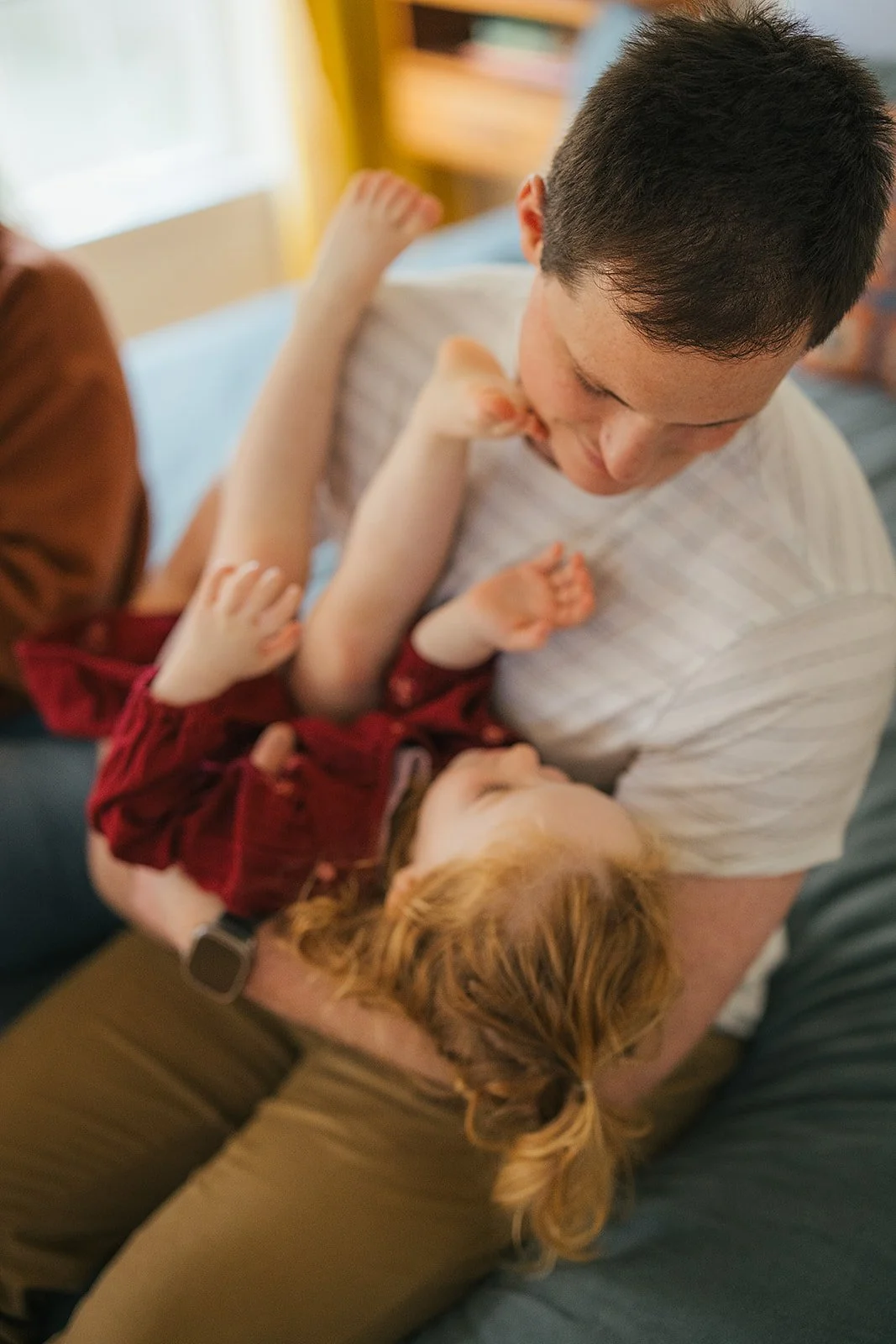 Dad playfully holds toddler daughter upside down on bed during Durham lifestyle family photography session