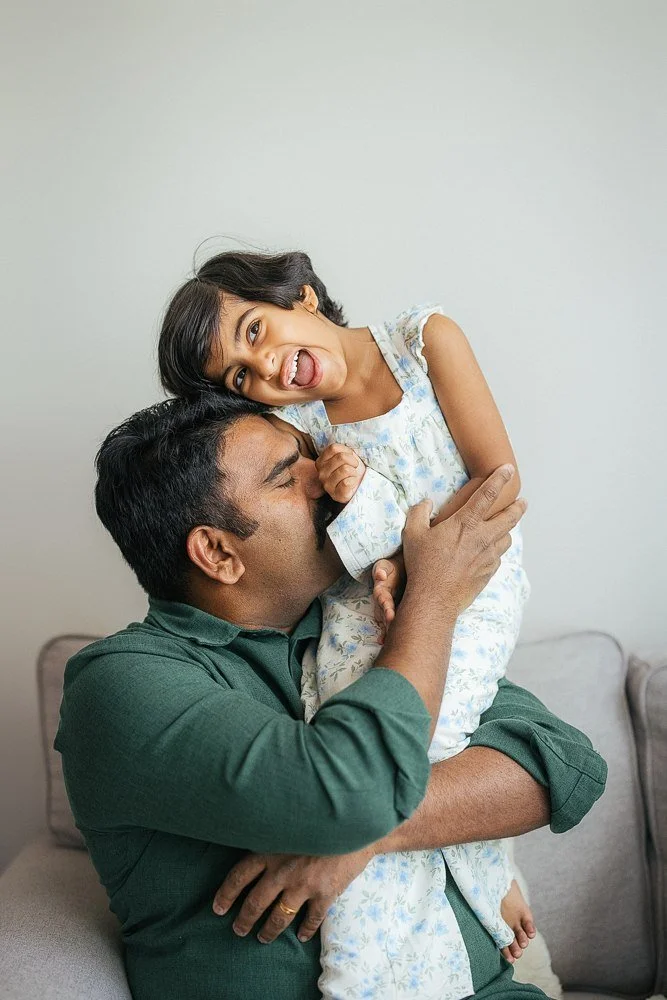 Father in a dark green shirt lifts his laughing daughter playfully — candid moment from an in-home family session in Apex, NC.