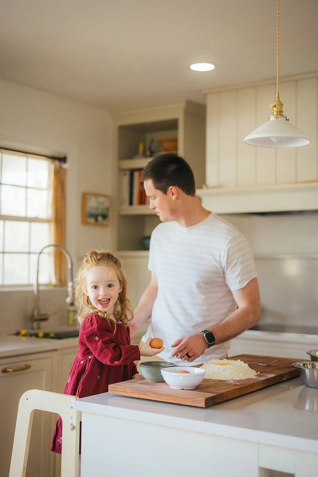 Toddler girl beams with joy while helping dad crack eggs during Durham in-home lifestyle family photography session