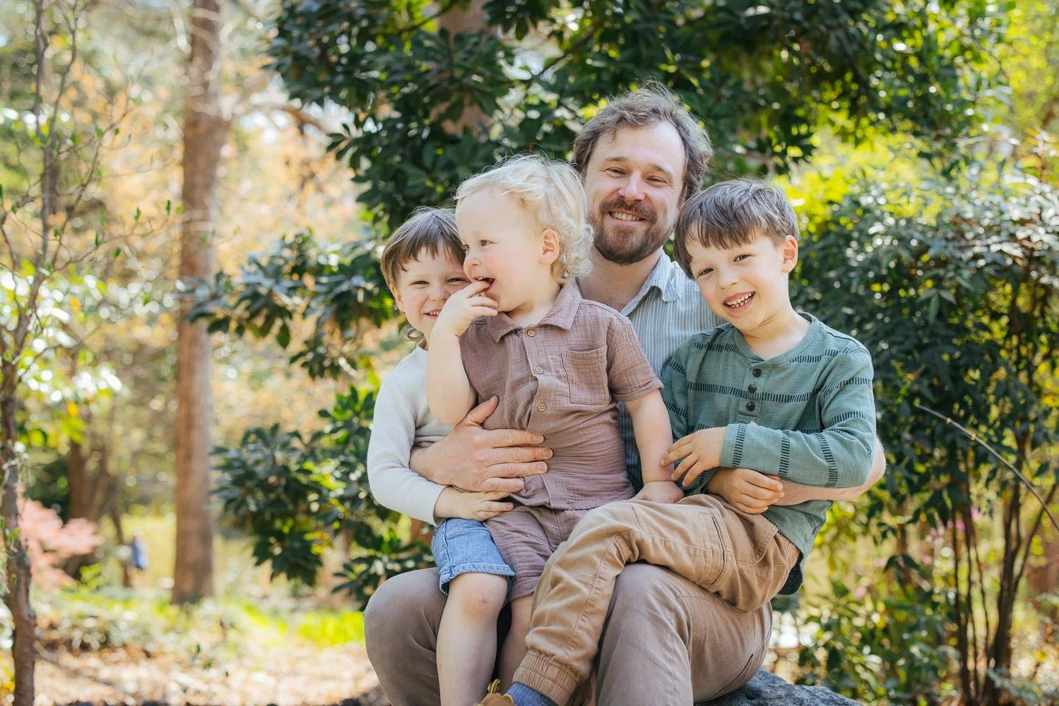 Dad hugging and laughing with his three sons in the dappled wooded garden at Duke Gardens Durham NC