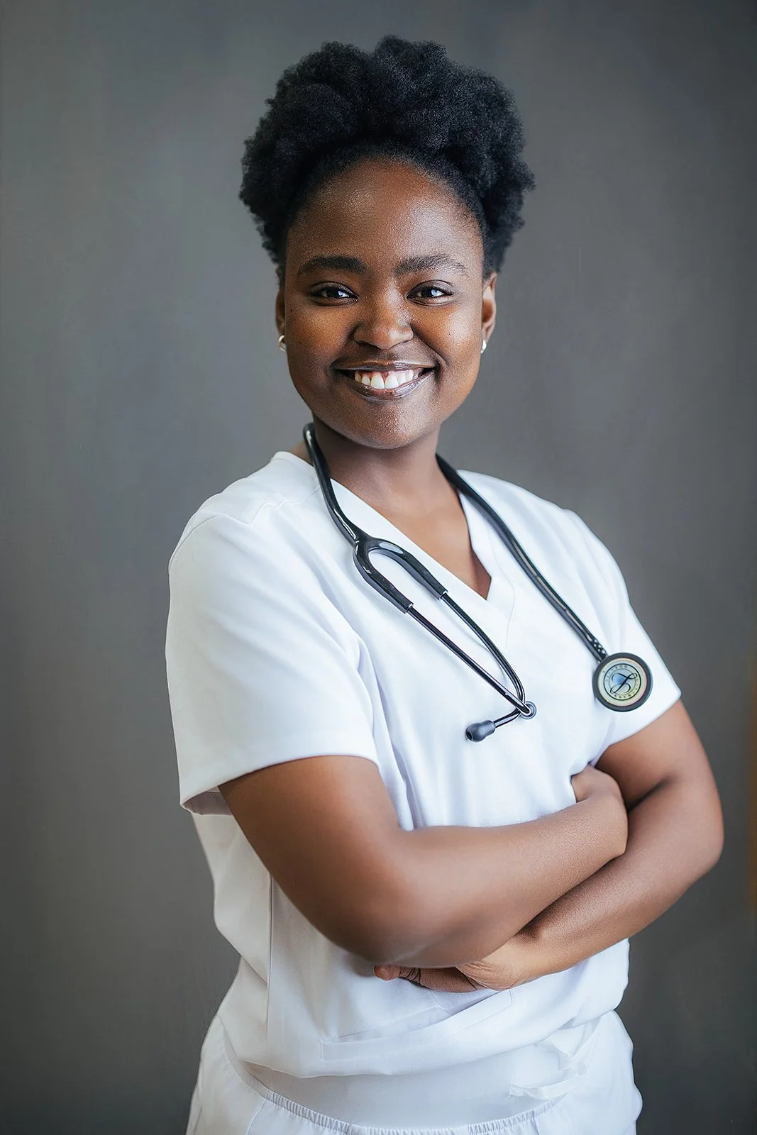 Durham Tech nursing student with natural hair, arms crossed and smiling confidently in white scrubs and black stethoscope, professional headshot Durham NC