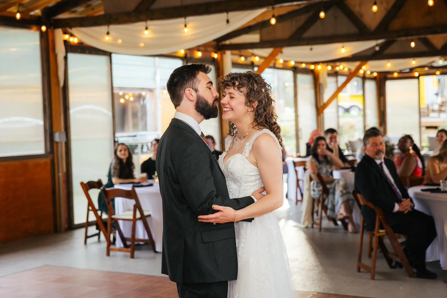 Bride and groom sharing their first dance in the reception pavilion at Honeysuckle Tea House Chapel Hill NC — string lights overhead and guests watching from tables