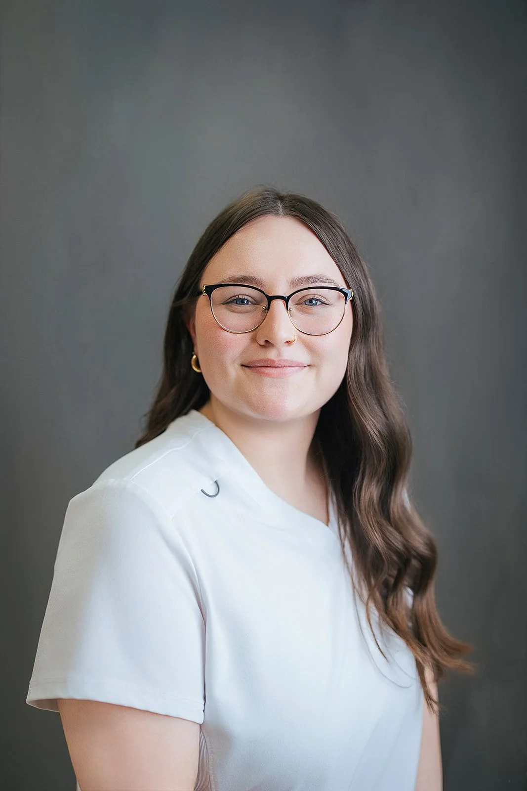 Durham Tech nursing student wearing glasses with long wavy dark hair, soft smile in white scrubs and red stethoscope, professional headshot in Durham