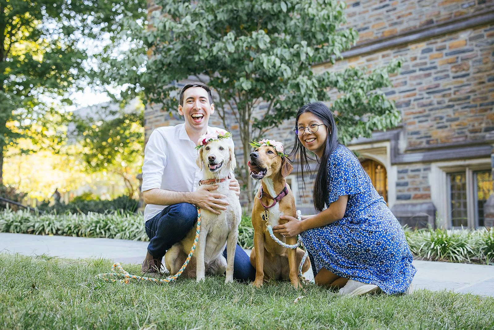A couple smiles with their dogs after their surprise engagement during a photoshoot at Duke Gardens in Durham, NC