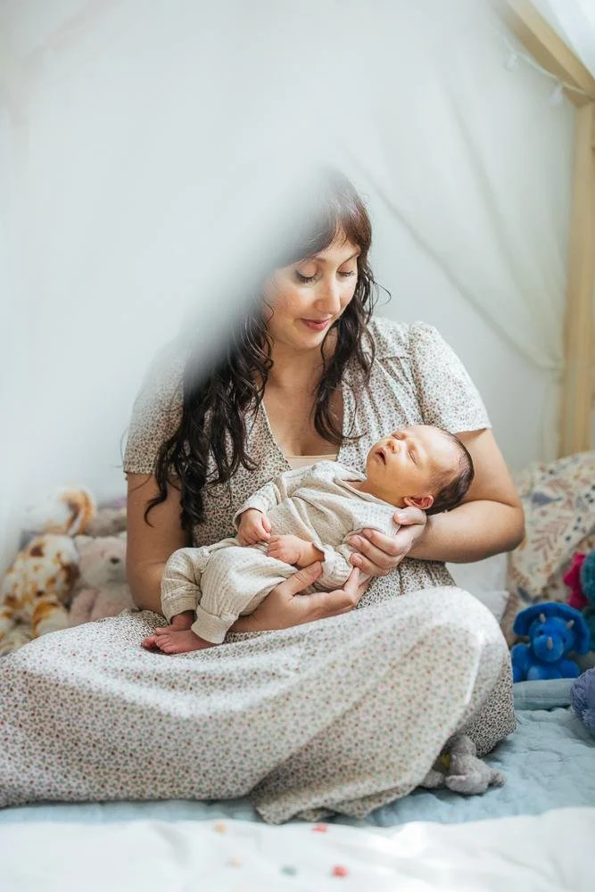 Mom sitting cross-legged inside a canopy tent cradling her newborn baby — Durham NC newborn photographer lifestyle session