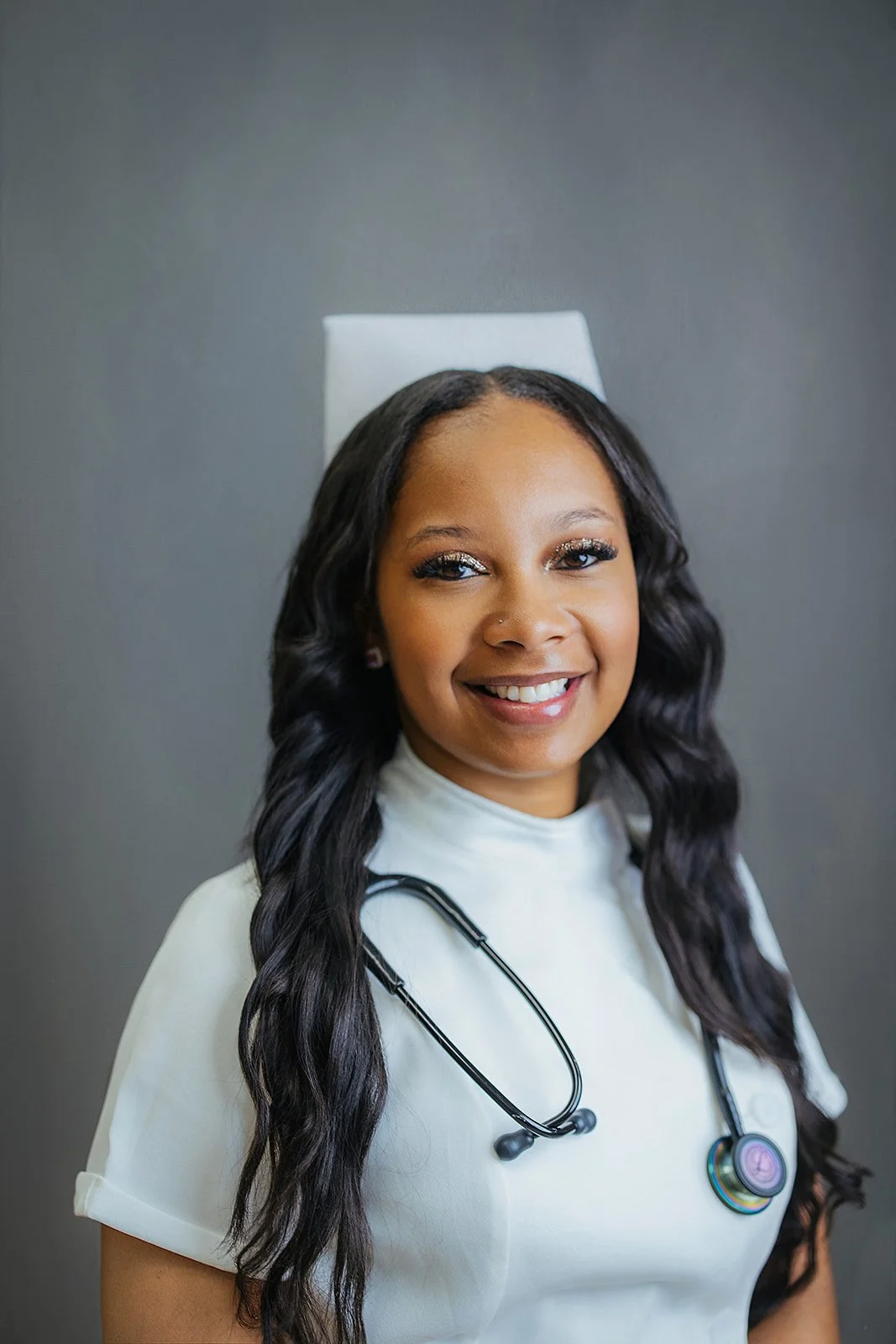 Durham Tech nursing student with long wavy hair and nurse cap, smiling in white scrubs and black stethoscope, professional headshot in Durham NC