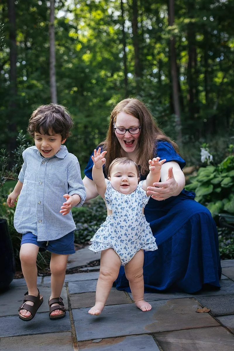 Mom celebrating as baby stands by themselves with toddler runs next to them