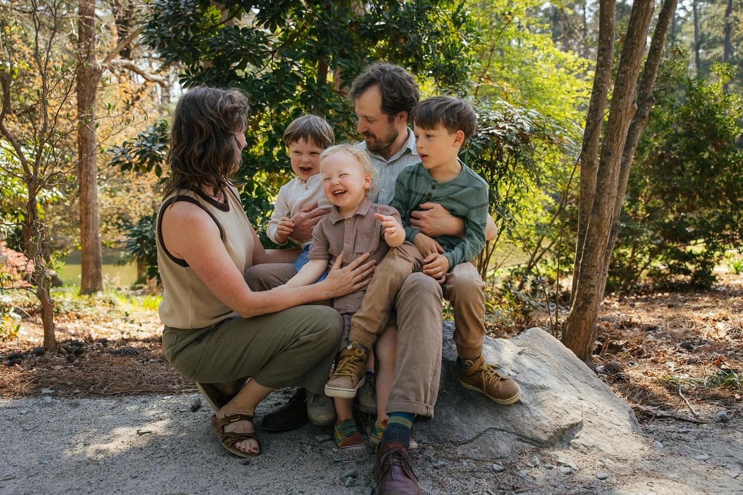 Family of five sitting together on rocks in the wooded garden section of Duke Gardens Durham NC — candid Durham NC family photographer