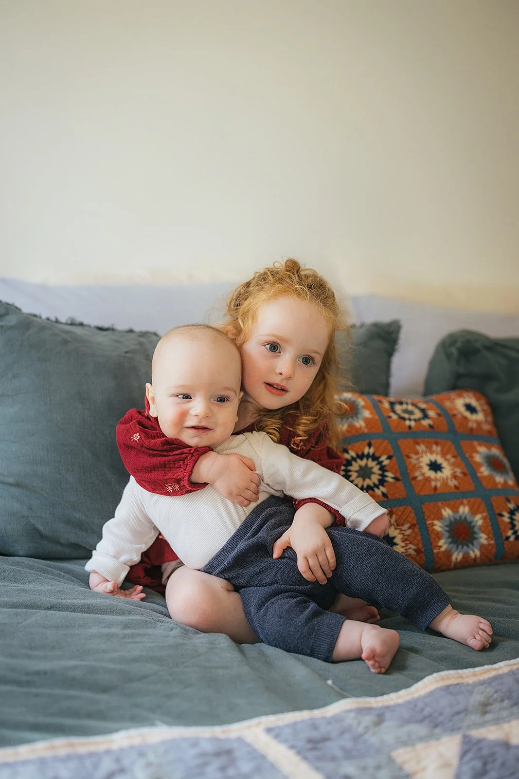 Toddler sister hugs baby brother in a sweet sibling portrait during Durham in-home family photography session
