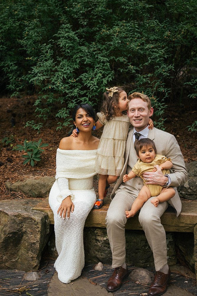 Family of four poses on a stone wall in Durham NC for a Duke Gardens family session