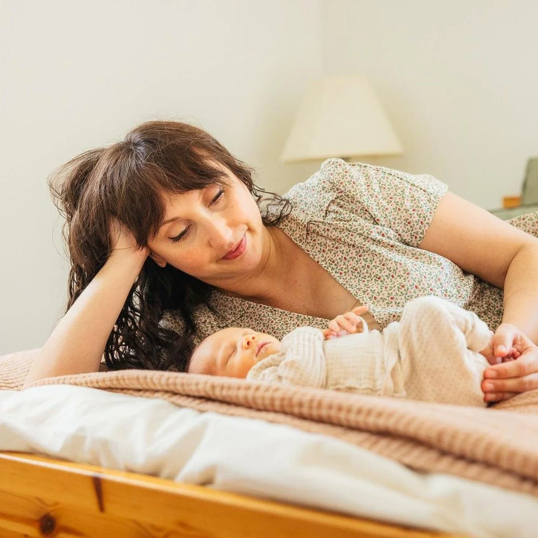 Mother smiles at her newborn baby while on a bed during a newborn photoshoot in Durham NC
