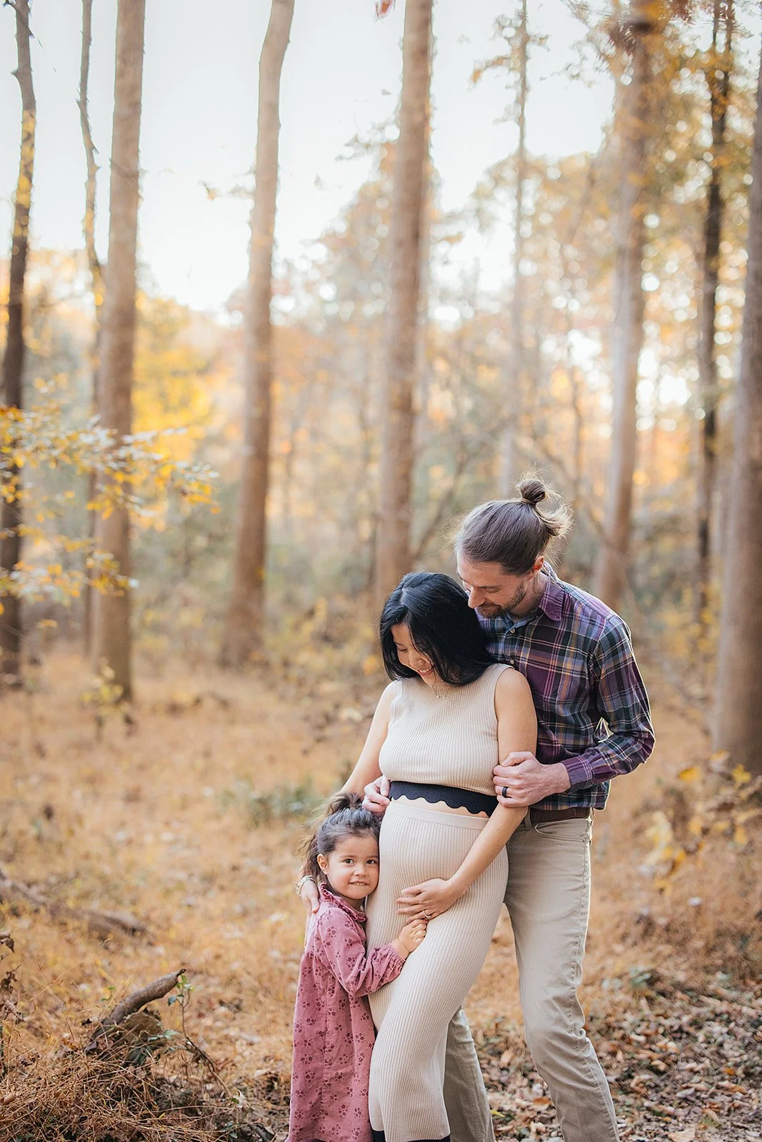 A pregnant woman poses with her family at a park for a maternity photoshoot