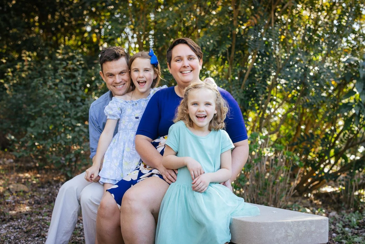 Family of four laughing together on a stone garden bench surrounded by lush green foliage at Duke Gardens Durham NC