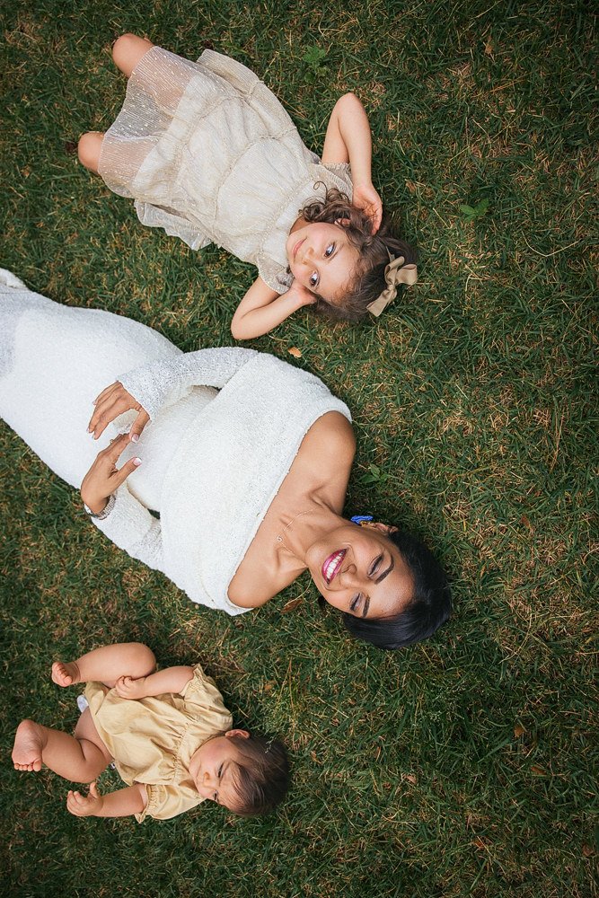 Mother smiles with two children laying in the grass for a Duke Gardens family portrait session in Durham, NC