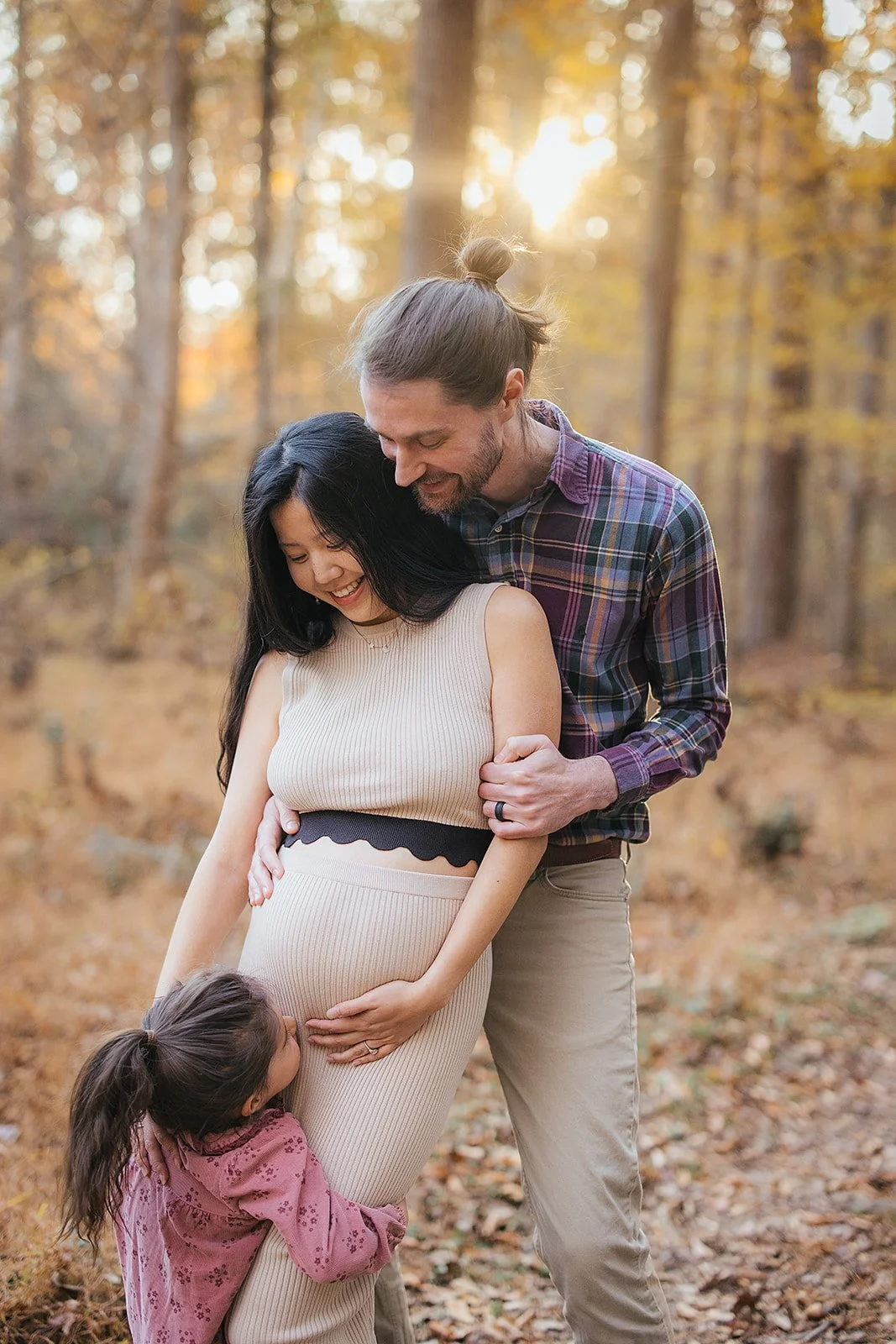 A pregnant woman poses with her family at the Eno River in Durham, NC for a maternity photoshoot