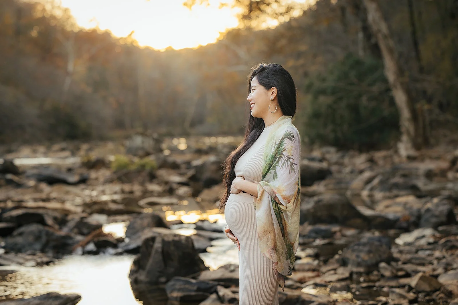 A pregnant woman looking out at the river at sunset during a maternity photography session in Durham, NC