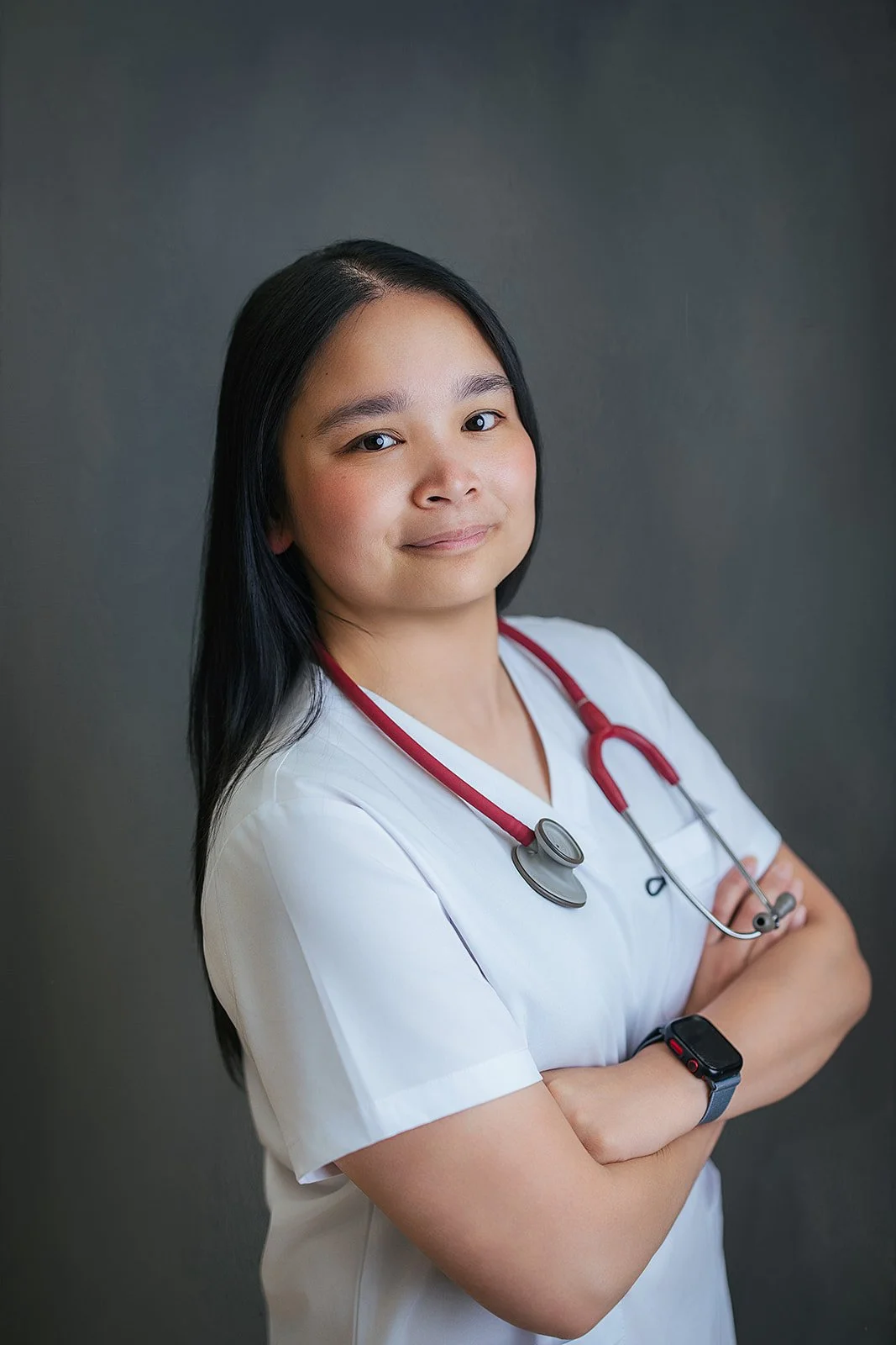 Durham Tech nursing student with long dark hair, arms crossed confidently in white scrubs and red stethoscope, professional headshot in Durham NC