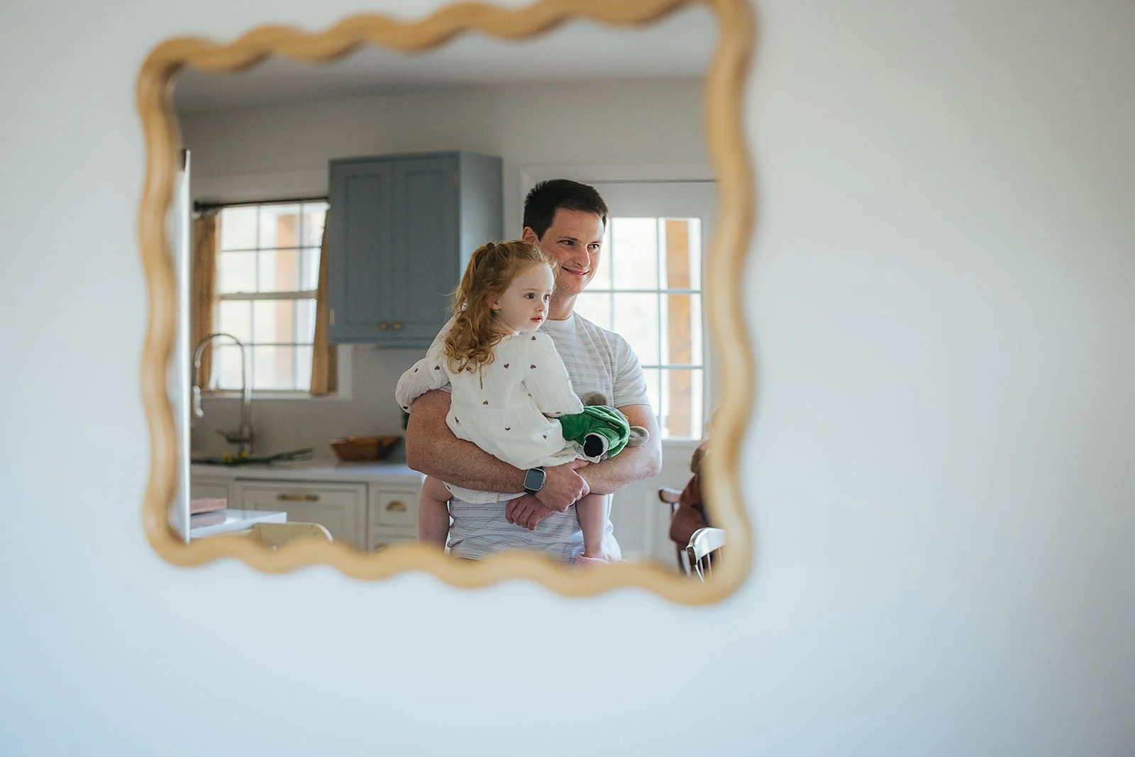 Dad and toddler daughter reflected in wavy decorative mirror during Durham in-home lifestyle family photography session