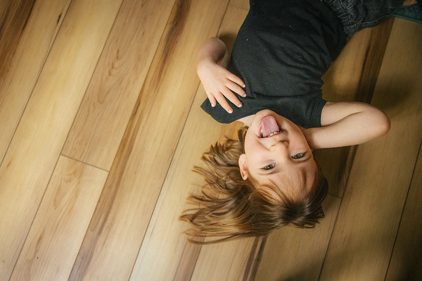 Young Girl Making Silly Face While Laying on Floor During In-Home Family Photography Session