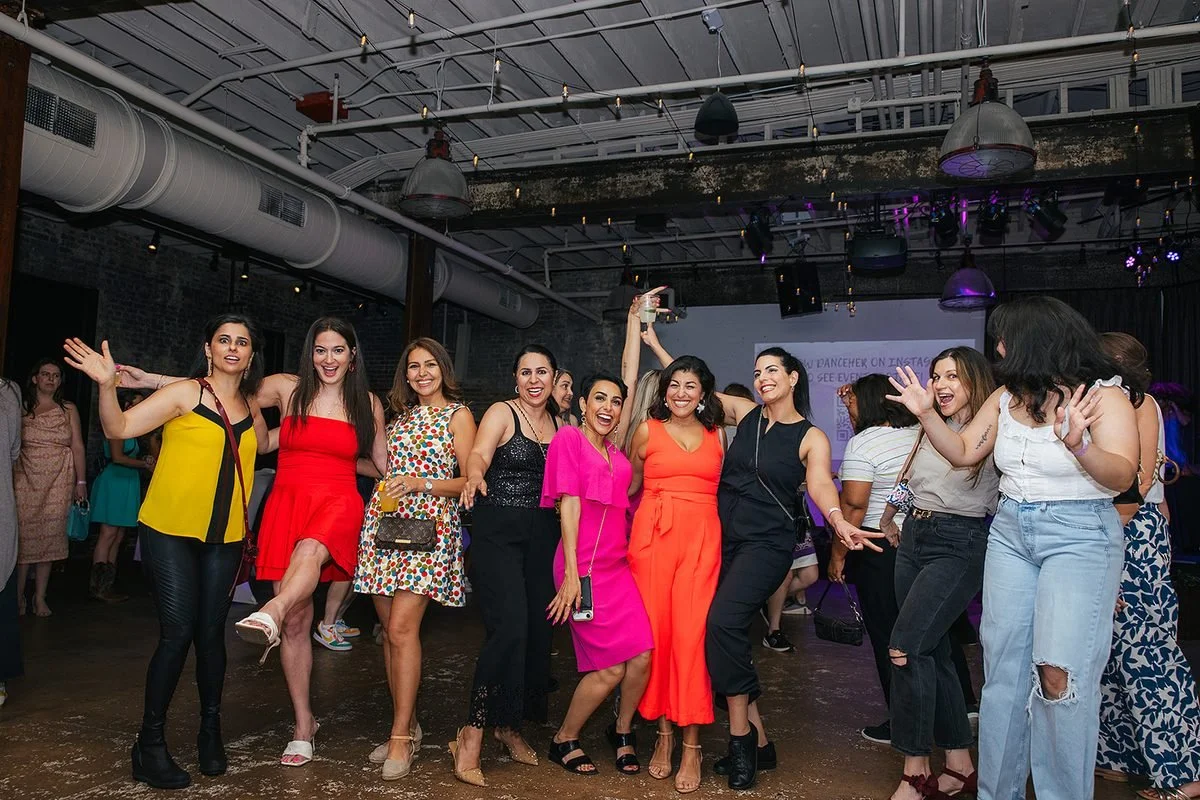 Large group of women cheering and posing together on the dance floor at Transfer Co Food Hall in Raleigh during the Dance Her popup event
