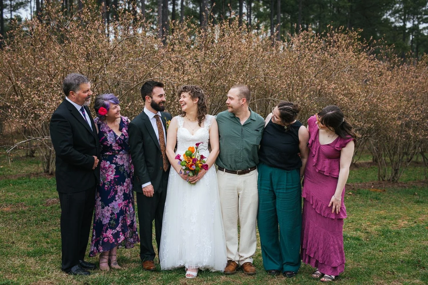 Family portrait of parents and siblings laughing together in front of bare winter trees on the farm at Honeysuckle Tea House in Chapel Hill NC wedding