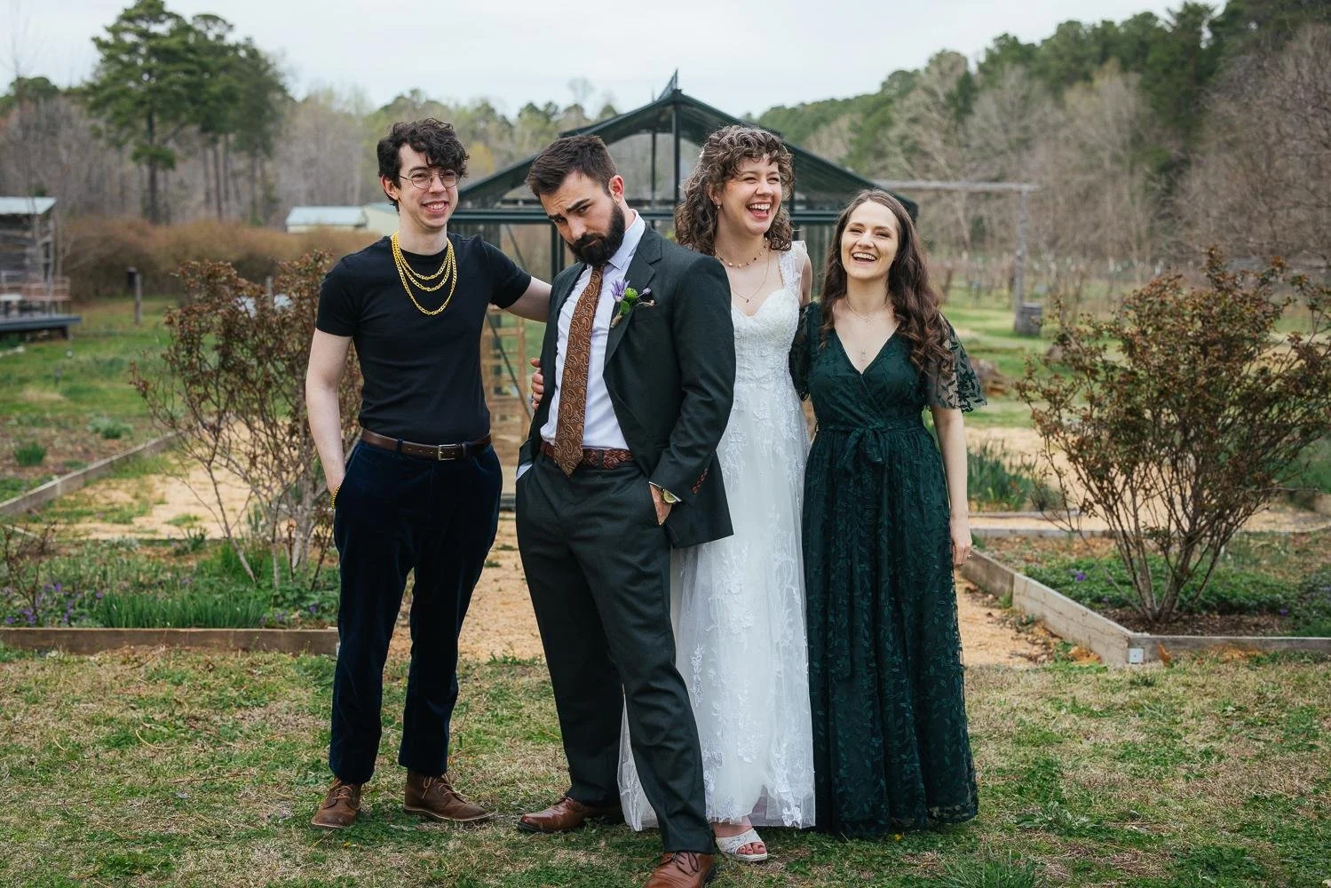 Bride and groom with siblings posing and laughing in a group portrait in front of the greenhouse at Honeysuckle Tea House Chapel Hill NC